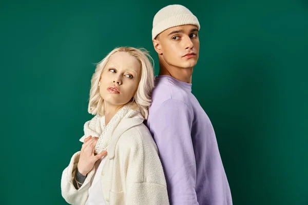 Tall man in hat and winter attire posing back to back with blonde woman on turquoise backdrop — Stock Photo