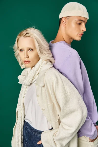 Блондинка в зимовому вбранні позує з рукою в кишені і назад з високим чоловіком на бірюзовому — стокове фото