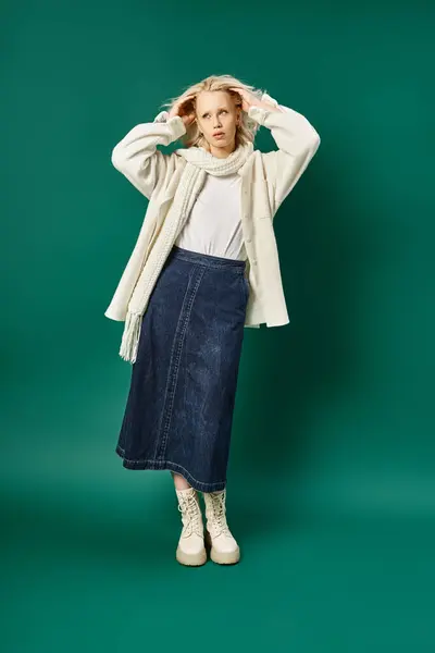 Полная длина блондинка в белой куртке и джинсовой юбке позируя на бирюзовой, зимняя мода — стоковое фото