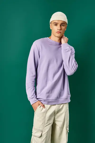Good looking man in beanie and purple sweatshirt posing with hand in pocket on turquoise backdrop — Stock Photo
