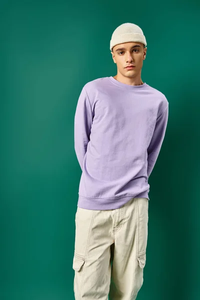 Bel homme en sweat-shirt violet et bonnet chaud posant sur fond turquoise, mode d'hiver — Photo de stock