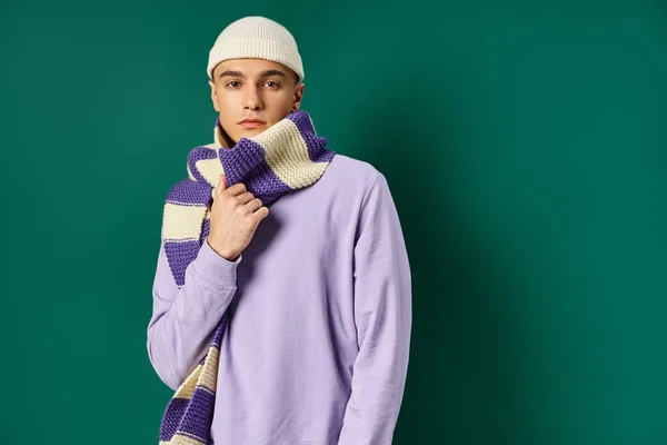 Bel homme en sweat-shirt violet, écharpe dénudée et bonnet posant sur fond turquoise — Photo de stock