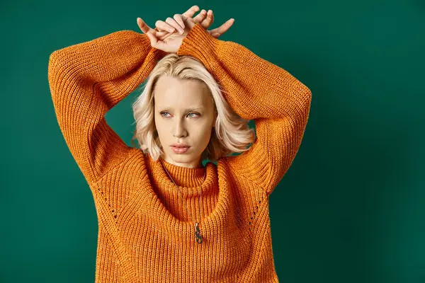 Young blonde woman in mustard yellow sweater posing with hands above head on turquoise backdrop — Stock Photo