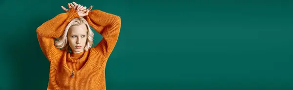 Young blonde woman in mustard yellow sweater posing with hands above head on turquoise, banner — Stock Photo