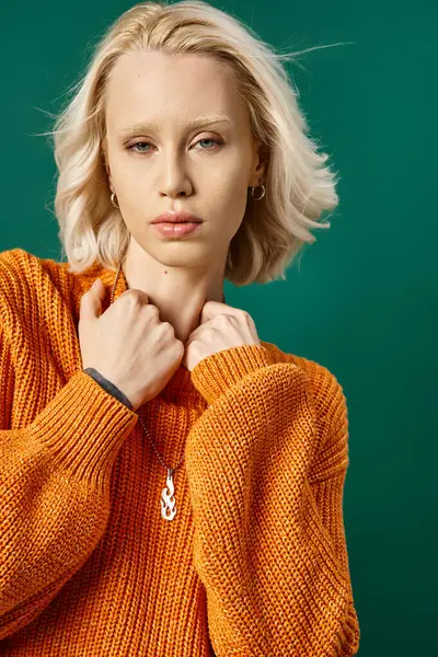 Attractive blonde woman in mustard yellow sweater posing on turquoise backdrop, winter fashion — Stock Photo