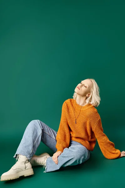 Woman in mustard yellow sweater and comfy denim jeans sitting on turquoise background, closed eyes — Stock Photo