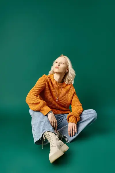 Dreamy woman in mustard yellow sweater and comfy denim jeans sitting on turquoise background — Stock Photo