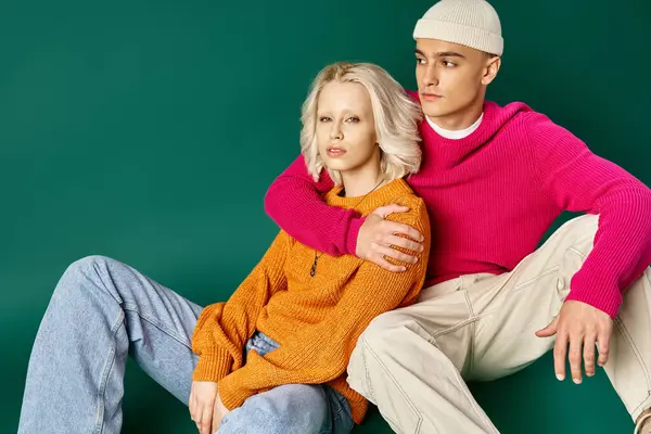 Couple in winter sweaters, man in beanie hugging blonde woman while sitting together on turquoise — Stock Photo