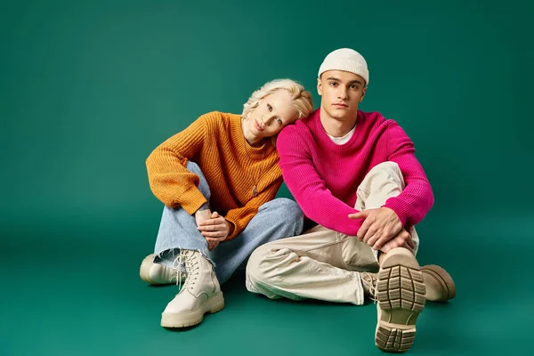 Couple en pulls, femme blonde penchée sur l'épaule de l'homme en bonnet sur turquoise, mode hiver — Photo de stock