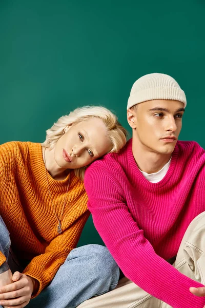 Young couple in sweaters, blonde woman leaning on shoulder of man in beanie, sitting on turquoise — Stock Photo