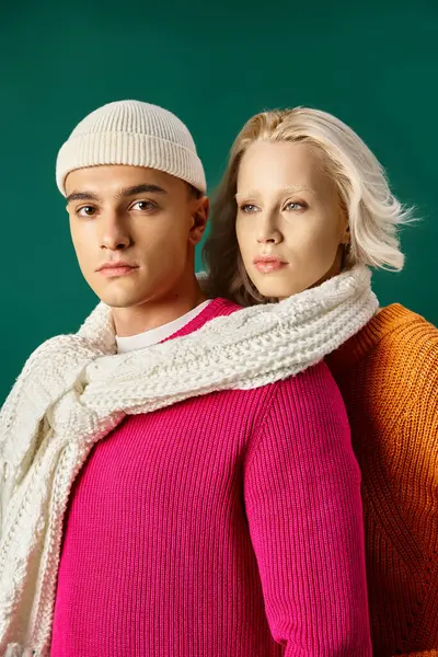 Pareja joven en suéteres compartiendo bufanda blanca y posando juntos en turquesa, moda de invierno - foto de stock