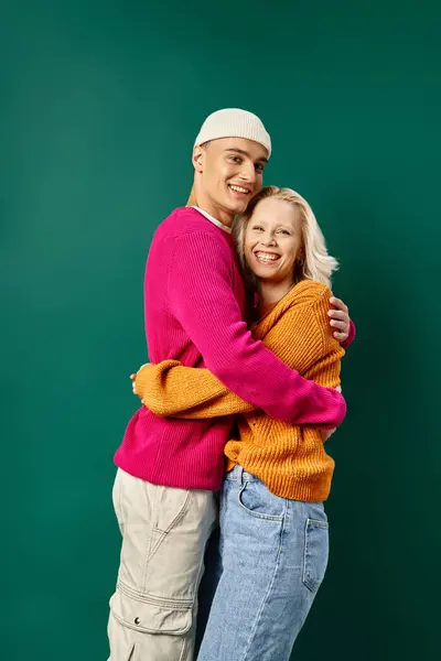 Joyful couple in winter attire, man in beanie hugging blonde girlfriend on turquoise, winter fashion — Stock Photo