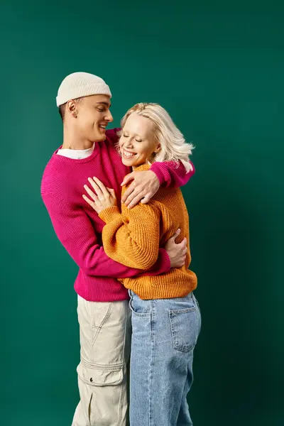 Couple in winter attire, man in beanie hugging happy girlfriend on turquoise, winter fashion — Stock Photo