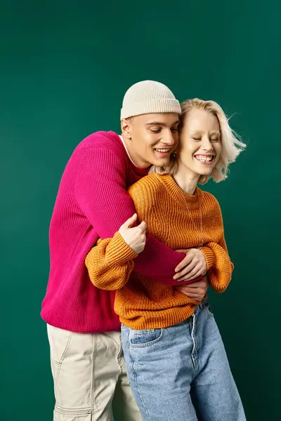 Couple in winter attire, man in beanie embracing happy girlfriend on turquoise, winter fashion — Stock Photo
