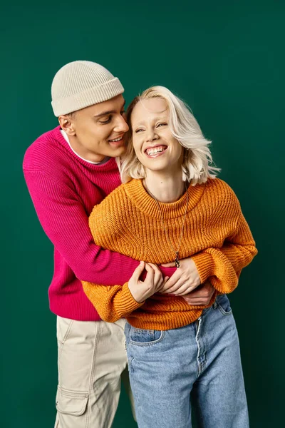 Couple in winter attire having fun, man in beanie embracing happy girlfriend on turquoise backdrop — Stock Photo