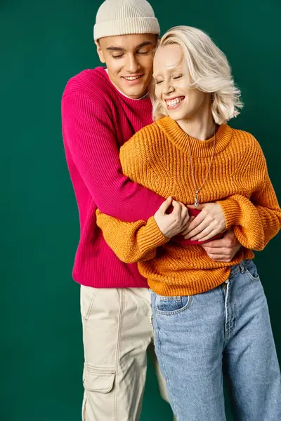 Happy couple in winter attire having fun, man in beanie embracing girlfriend on turquoise backdrop — Stock Photo