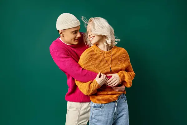 Cheerful couple in winter attire having fun, man in beanie hugging girlfriend on turquoise backdrop — Stock Photo