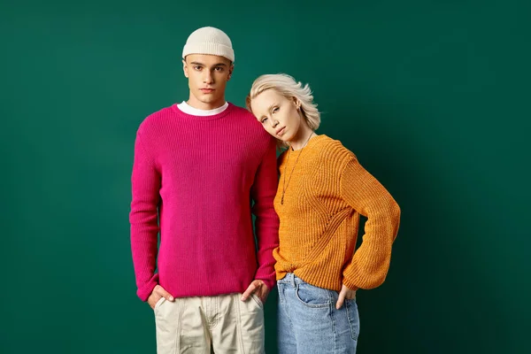 Fashionable couple in fashionable outfits posing with hands in pockets on turquoise background — Stock Photo