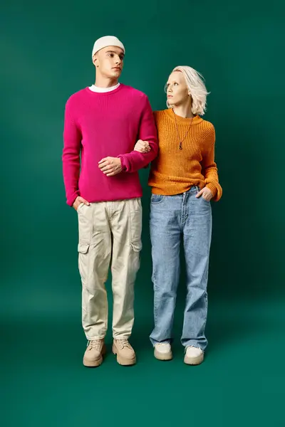 Hombre y mujer de moda en trajes de invierno posando con las manos en bolsillos sobre fondo turquesa - foto de stock