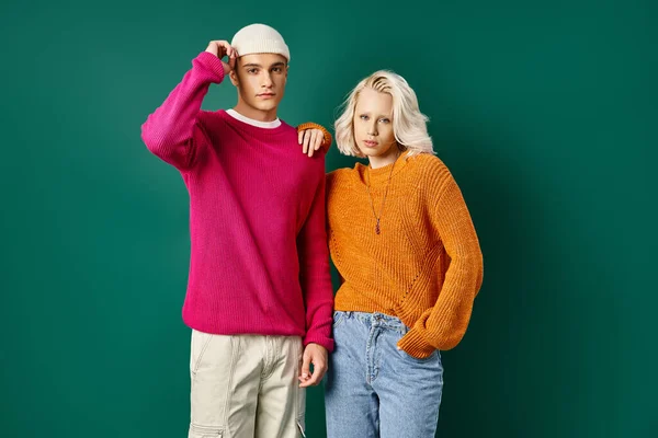 Modischer Mann und blonde Frau in winterlichen Outfits posieren gemeinsam auf türkisfarbenem Hintergrund — Stockfoto