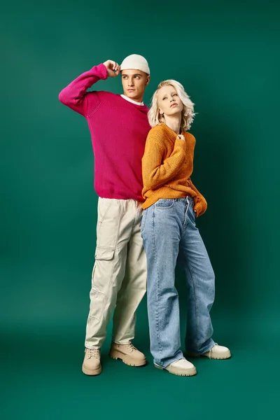 Modische Models in winterlichen Outfits posieren gemeinsam auf türkisfarbenem Hintergrund, junges stylisches Paar — Stockfoto