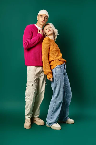Longitud completa de elegante pareja joven en suéteres de invierno posando juntos sobre fondo turquesa - foto de stock