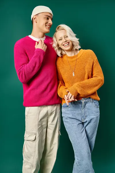 Cheerful young couple in winter sweaters laughing and looking at camera on turquoise background — Stock Photo