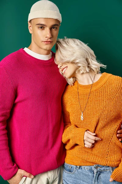 Happy blonde woman leaning on handsome boyfriend in sweater on turquoise background, young couple — Stock Photo