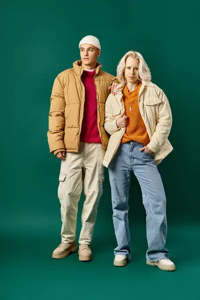 Пара в зимних куртках puffer позировать вместе на бирюзовом фоне, стильный мужчина и женщина — стоковое фото