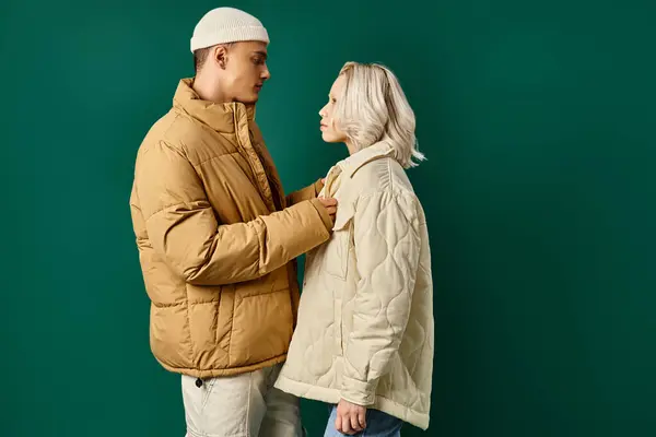 Caring man wearing puffer jacket on blonde girlfriend on turquoise background, winter fashion — Stock Photo