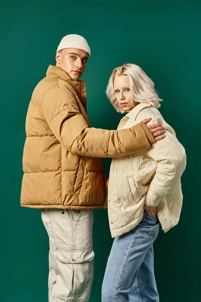 Stylish couple in puffer jackets posing together on turquoise background, young man and woman — Stock Photo