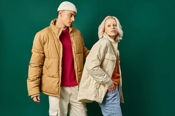 Young couple in puffer jackets posing together on turquoise background, fashionable man and woman — Stock Photo