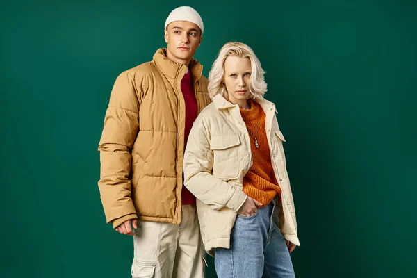 Young man and woman in puffer jackets posing together on turquoise background, stylish couple — Stock Photo
