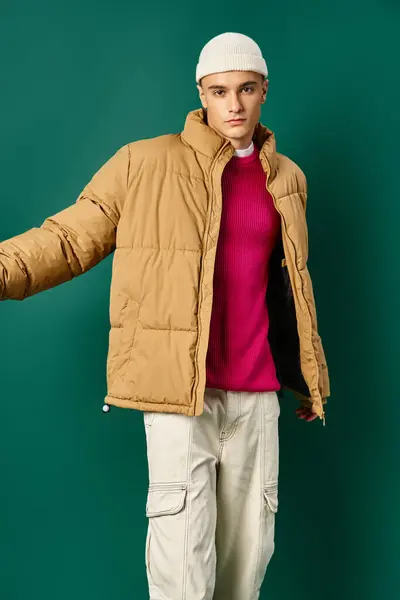 Stylischer Mann mit Mütze und Winterjacke posiert auf türkisfarbenem Hintergrund, Wintertrends — Stockfoto