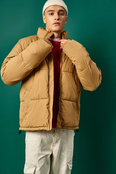 Giovane uomo in cappello beanie indossa giacca elegante soffietto su sfondo turchese, tendenze invernali — Foto stock
