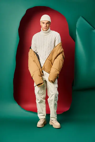 Stylish man in beanie, white sweater and puffer jacket on ripped red with turquoise backdrop — Stock Photo