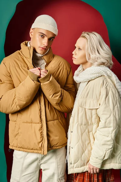 Junge blonde Frau in Winterjacke und Strickschal schaut Mann auf Rot mit türkisfarbenem Hintergrund an — Stockfoto