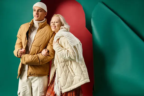 Happy couple in stylish winter jackets smiling and posing together on red with turquoise backdrop — Stock Photo