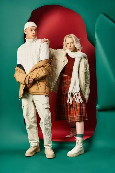 Stilvolles Paar in Winterjacken posiert gemeinsam auf rotem mit türkisfarbenem Hintergrund — Stockfoto