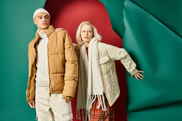 Stylish young man and woman in winter jackets posing together on red with turquoise backdrop — Stock Photo