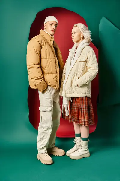 Full length of couple in modern winter jackets posing together on red with turquoise backdrop — Stock Photo