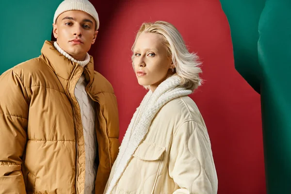 Ritratto di coppia in giacche invernali posa con le mani in tasche su sfondo rosso turchese — Foto stock