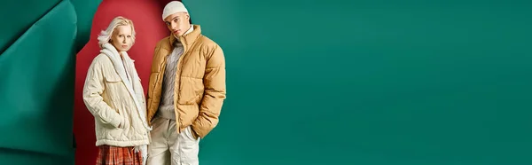 Banner of couple in winter jackets posing with hands in pockets on red with turquoise backdrop — Stock Photo