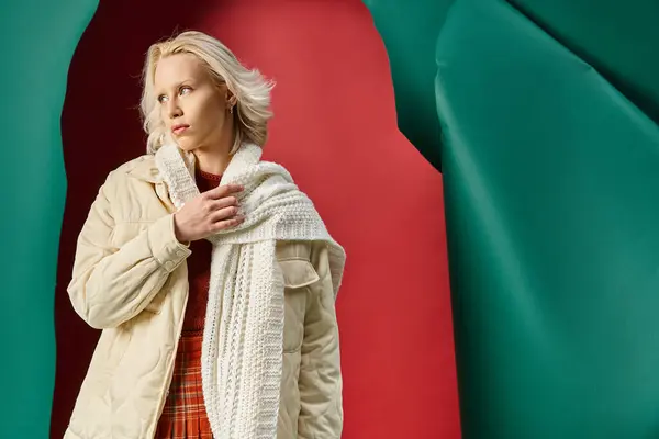 Jovem mulher loira em casaco de inverno ajustando lenço de malha em vermelho com fundo turquesa — Fotografia de Stock