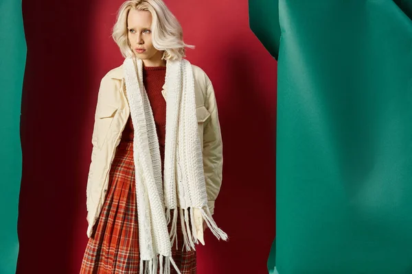 Atractiva mujer rubia en traje de invierno posando en chaqueta blanca sobre rojo con telón de fondo turquesa - foto de stock