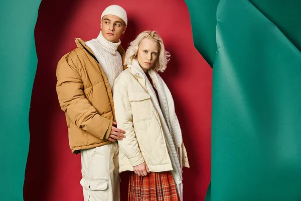 Hombre y mujer con estilo en chaquetas de invierno posando juntos sobre fondo rojo y turquesa desgarrado - foto de stock