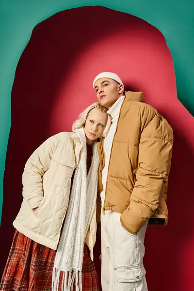 Молодая романтическая пара в зимних нарядах, стоящая рядом с разорванной бирюзой и красным фоном — стоковое фото