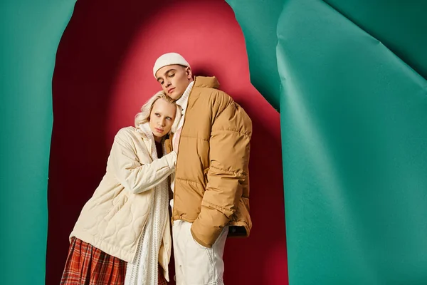 Young romantic couple in winter attire standing together near torn turquoise and red background — Stock Photo