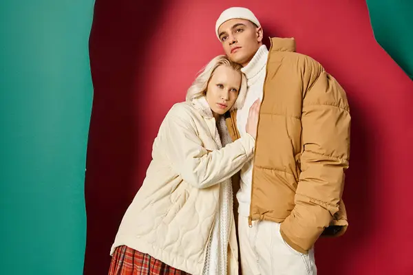 Jovem casal romântico em casacos de inverno de pé juntos perto rasgado turquesa e fundo vermelho — Fotografia de Stock