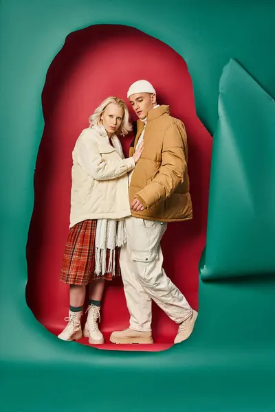 Woman in outerwear and plaid skirt posing with boyfriend near torn turquoise and red backdrop — Stock Photo